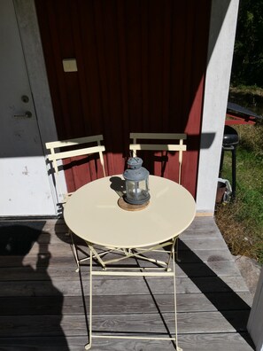 A round table with a lantern on top, set on a wooden deck with white chairs.