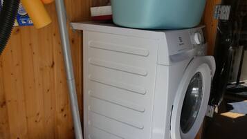 Un espace réduit dédié à la buanderie, comprenant un lave-linge, un aspirateur et un évier bleu posé sur un meuble en bois.