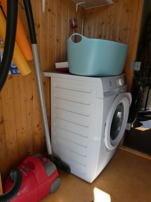 Een kleine wasruimte met een wasmachine, een stofzuiger en een blauwe wasbak op een houten kastje.