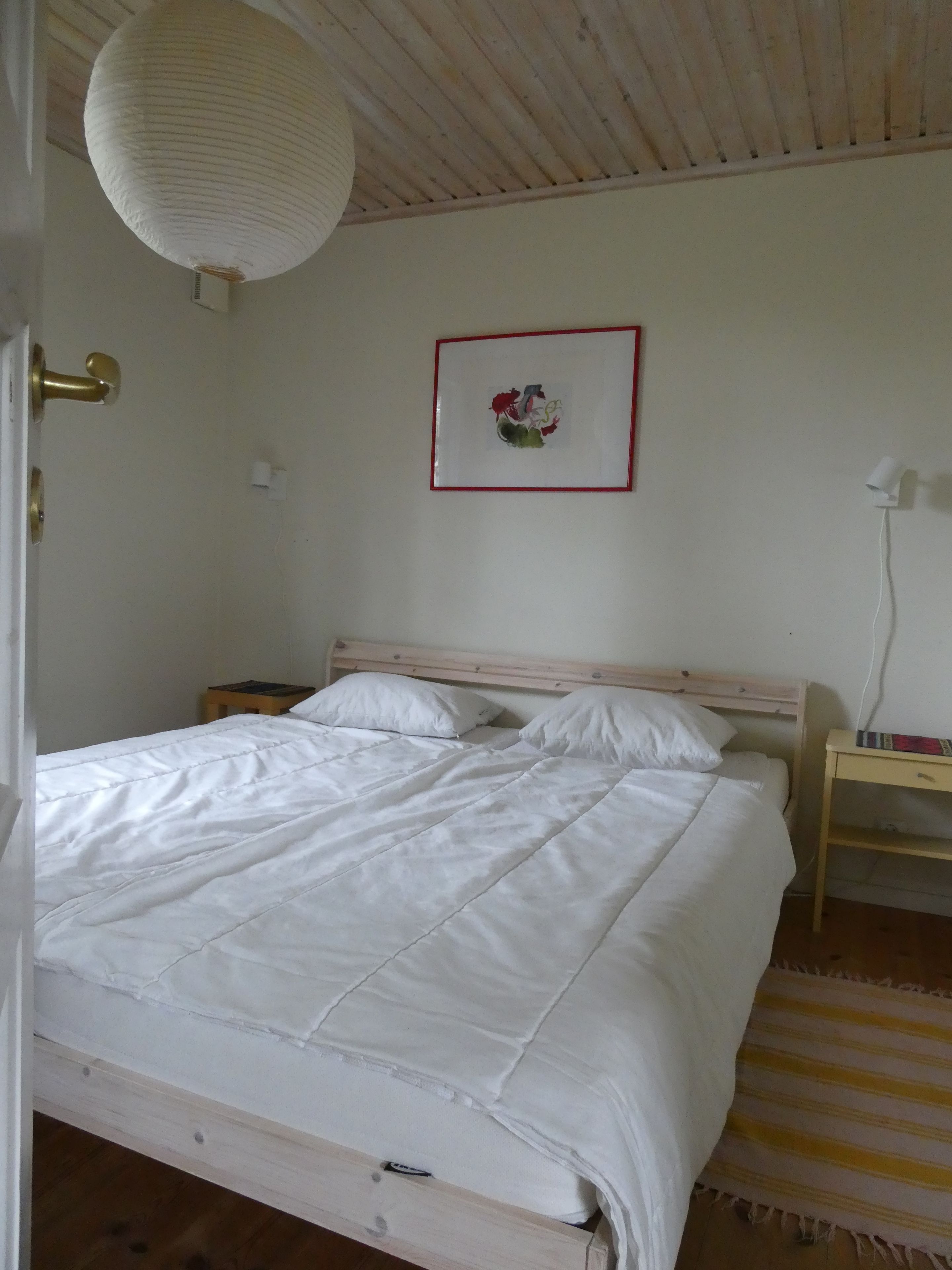 Ett sovrum med en säng, ett sängbord, en vägglampa och en inramad tavla.