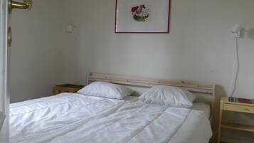 Ett sovrum med en säng, ett sängbord, en vägglampa och en inramad tavla.