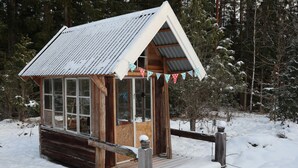 Uma cabana de madeira com telhado de metal, rodeada por árvores cobertas de neve.