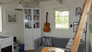 Ett mysigt vardagsrum med en grå soffa, en gitarr i trä, en bokhylla och ett fönster med utsikt över grönskan.