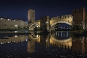 Eine Steinbrücke mit Bögen über einem ruhigen Fluss, der Brücke und die umliegende Bebauung spiegelt.