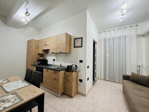 Ein kompakter Wohnraum mit Küchenzeile, Essbereich und einer Sitzecke mit Sofa und Vorhängen.