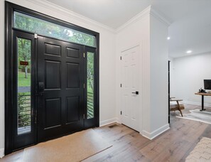Un interior moderno con una puerta negra, paredes blancas y suelo de madera.