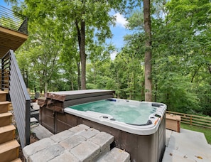 Un jacuzzi en zona boscosa con terraza de madera y escalones que lo conducen.