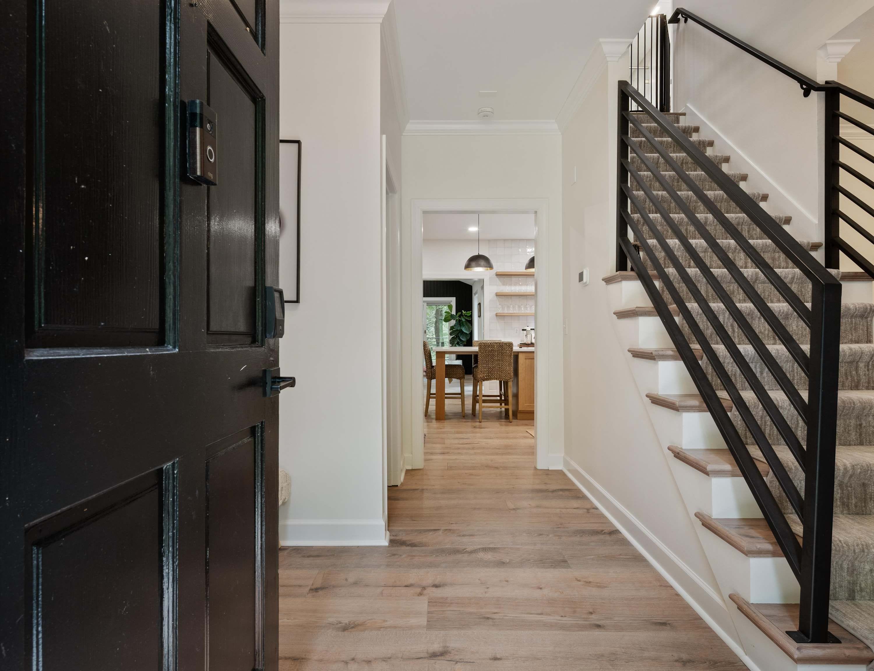 A hallway with a wooden floor leading to a staircase with a black handrail.
