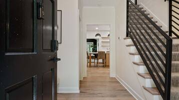 A hallway with a wooden floor leading to a staircase with a black handrail.