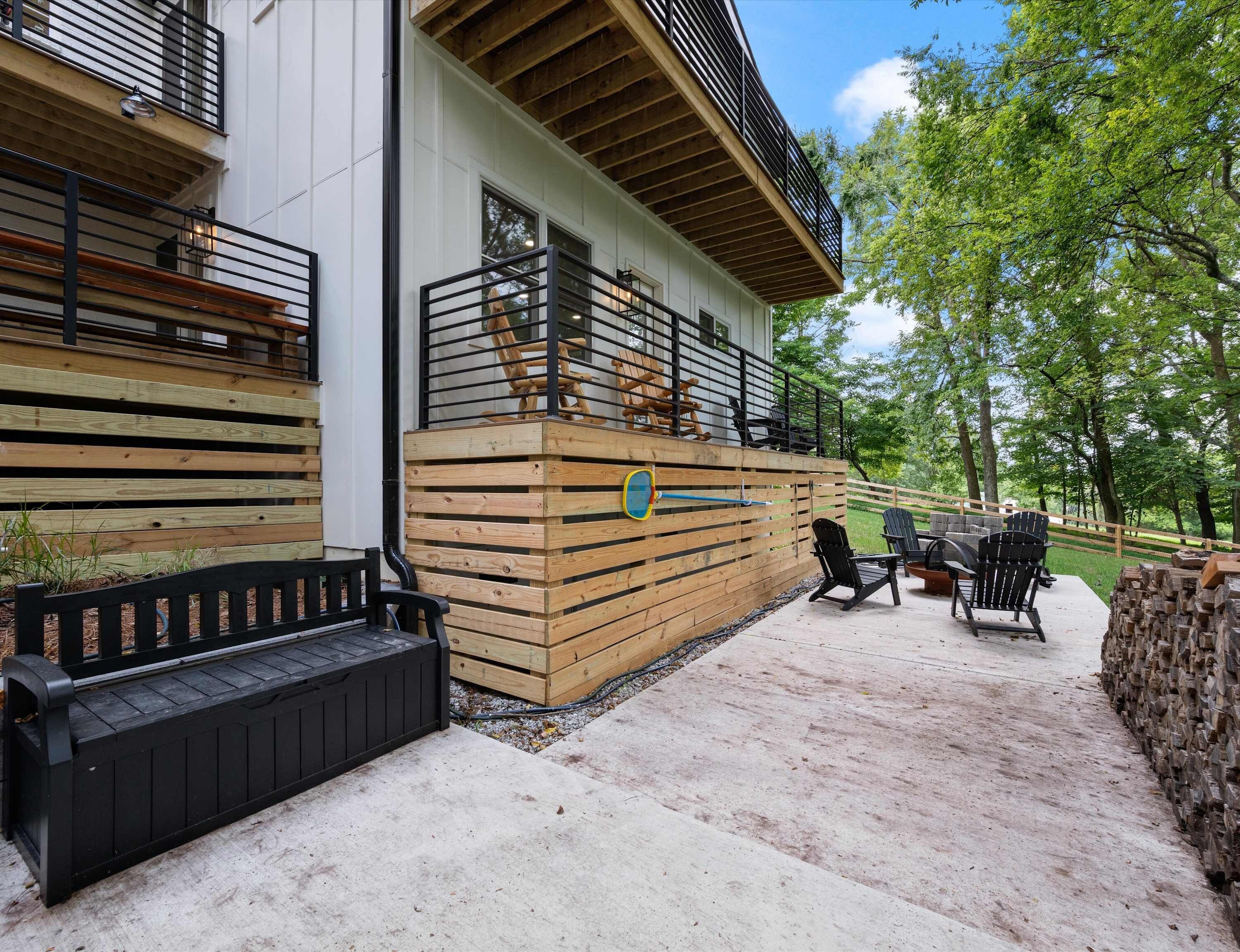 Een modern gebouw met een houten terras, buitenmeubels en uitzicht op de omliggende bomen.