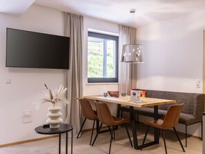 A modern dining area with a table, chairs, a flat-screen TV, and a window with curtains. - Holiday Apartment for 6 People & Infinity Pool (Sankt Martin am Tennengebirge)