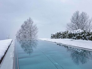 A clear indoor swimming pool with a glass floor, surrounded by snow-covered trees and bushes. - Holiday Apartment for 6 People & Infinity Pool (Sankt Martin am Tennengebirge)