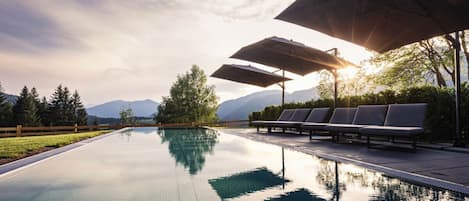 A swimming pool with lounge chairs and umbrellas, surrounded by trees and mountains in the background.
