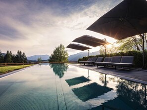 A swimming pool with lounge chairs and umbrellas, surrounded by trees and mountains in the background. - Holiday Apartment for 6 People & Infinity Pool (Sankt Martin am Tennengebirge)