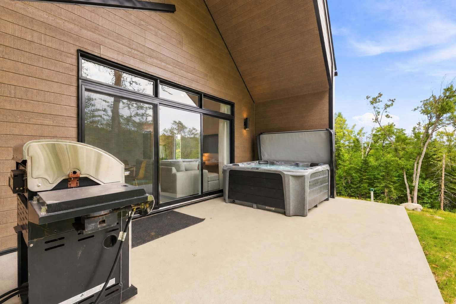 A patio with a grill, a hot tub, and a sliding glass door leading to a covered outdoor area.