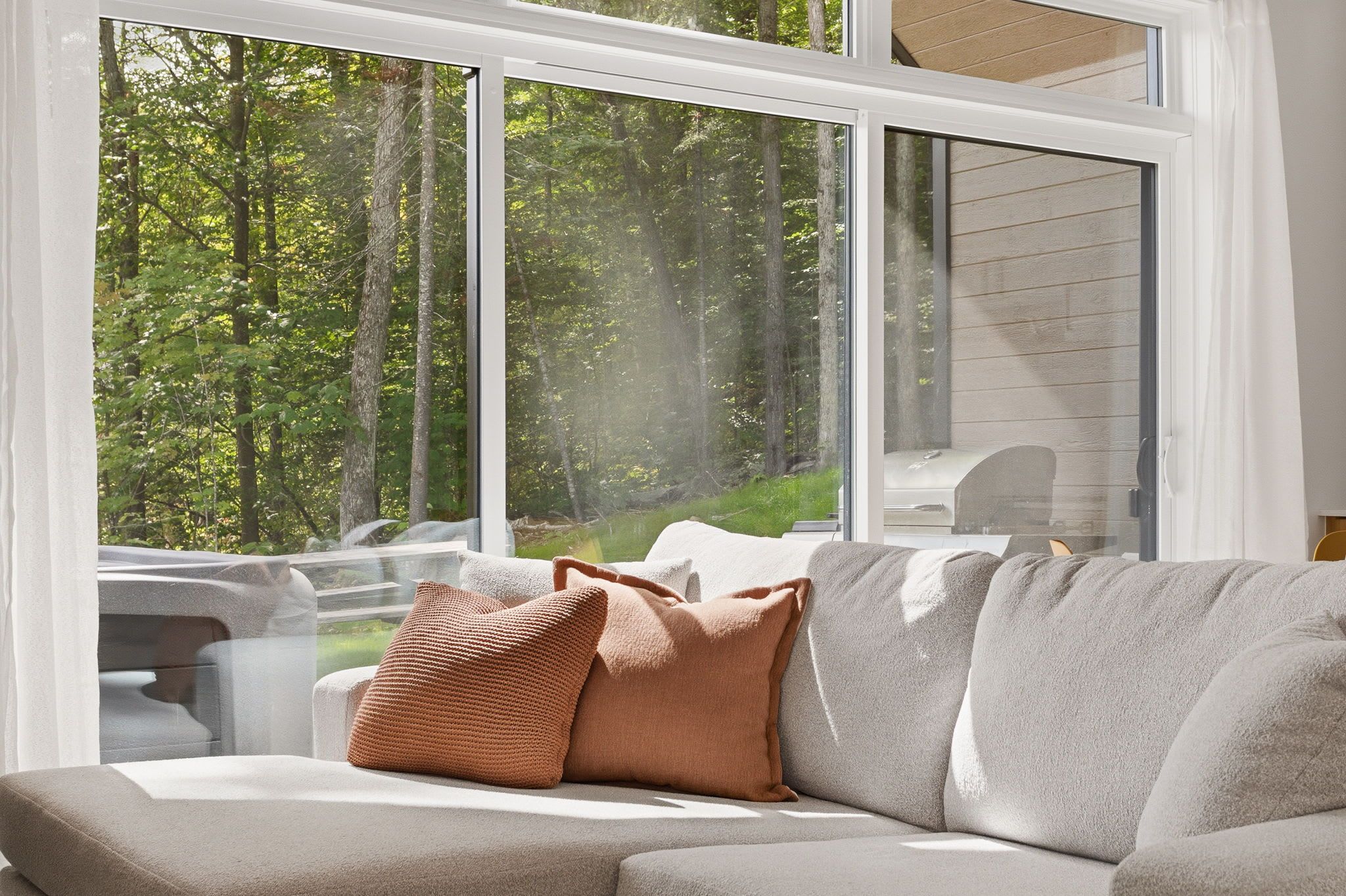 A modern living room with a large window, a sofa, and a grill outside.