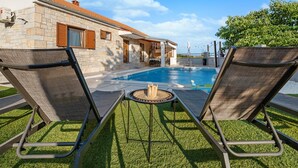 A poolside area with two lounge chairs, a small table, and a stone building in the background. - Villa Niko Dalmatia - Two Bedroom Villa, Sleeps 4 (Raštević)