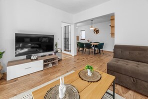 Ein modernes Wohnzimmer mit Flachbildfernseher, Holzboden, einem braunen Sofa und einem Essbereich mit Tisch und Stühlen.