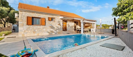 Une maison en pierre avec un toit en tuiles, une piscine et un jardin agrémenté de graviers blancs.