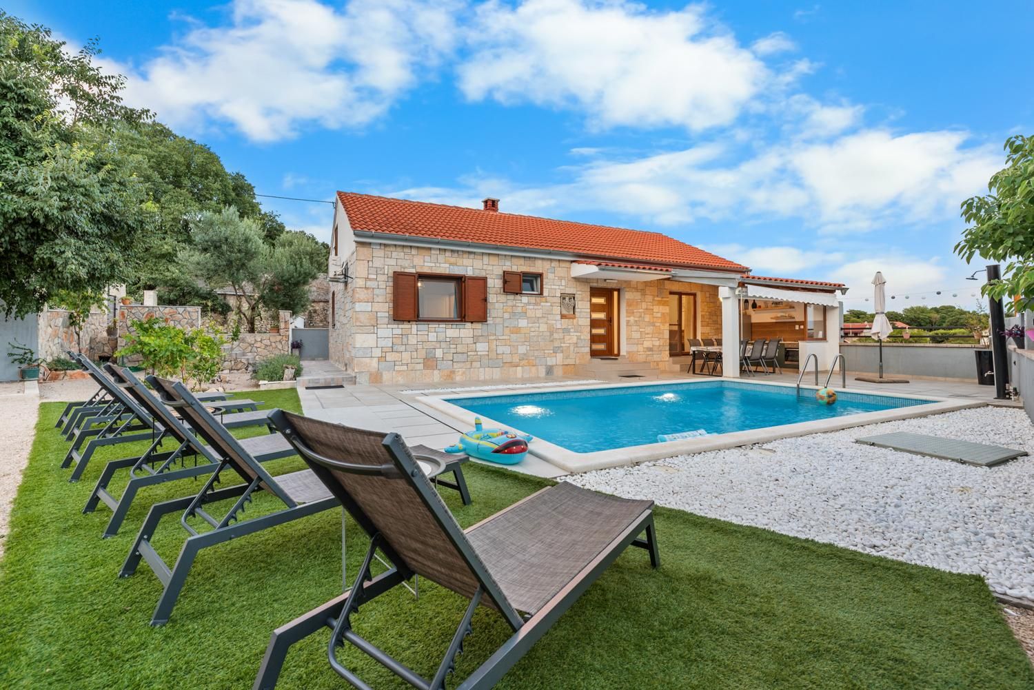 A house with a swimming pool, outdoor seating, and a stone facade.