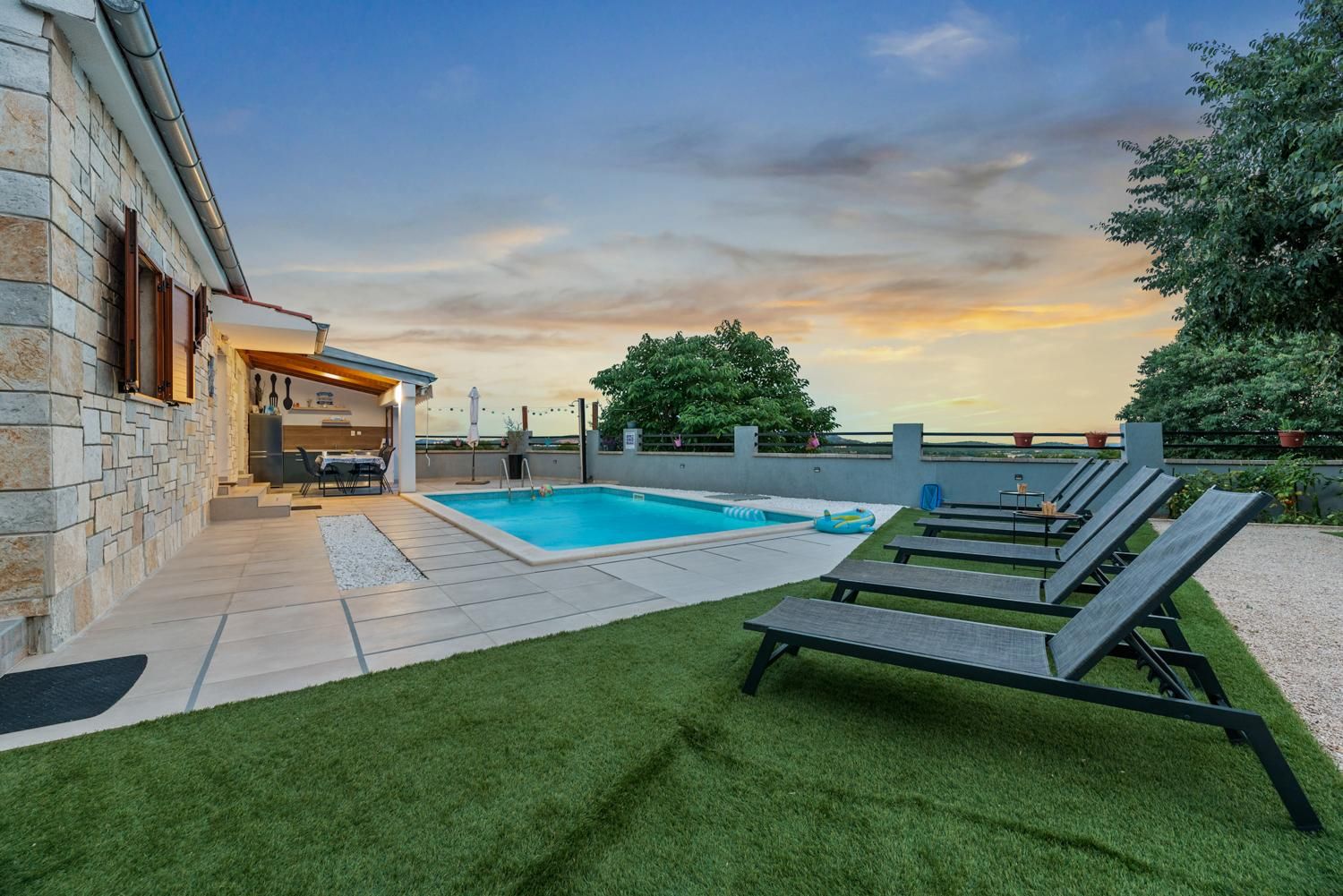 Un patio trasero con piscina, sillas de descanso y un área de patio con mobiliario exterior.