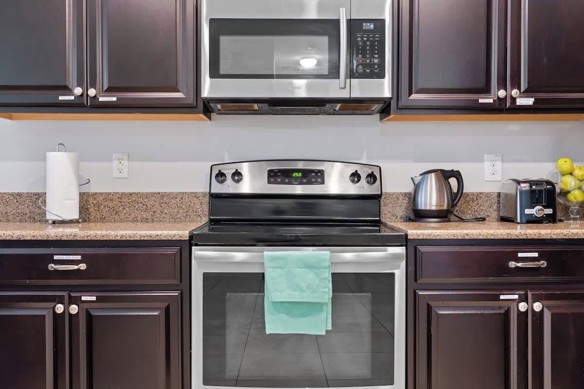 Una cocina con armarios de madera oscura, un microondas de acero inoxidable, una estufa y un tostador.