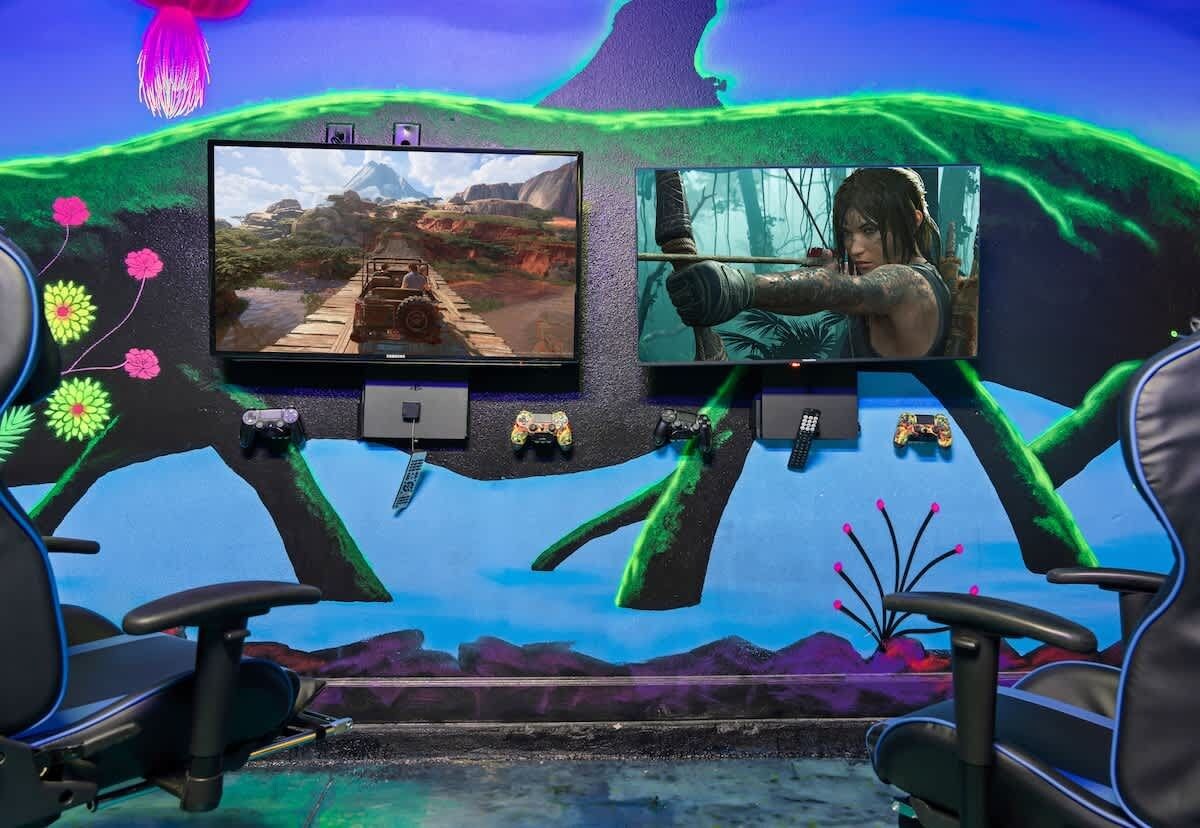 A gaming setup with two monitors, gaming chairs, and a wall mural.