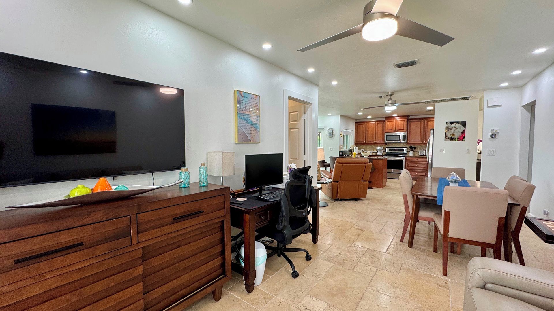 A modern living room with a flat-screen TV, wooden entertainment unit, and a dining area with a table and chairs.