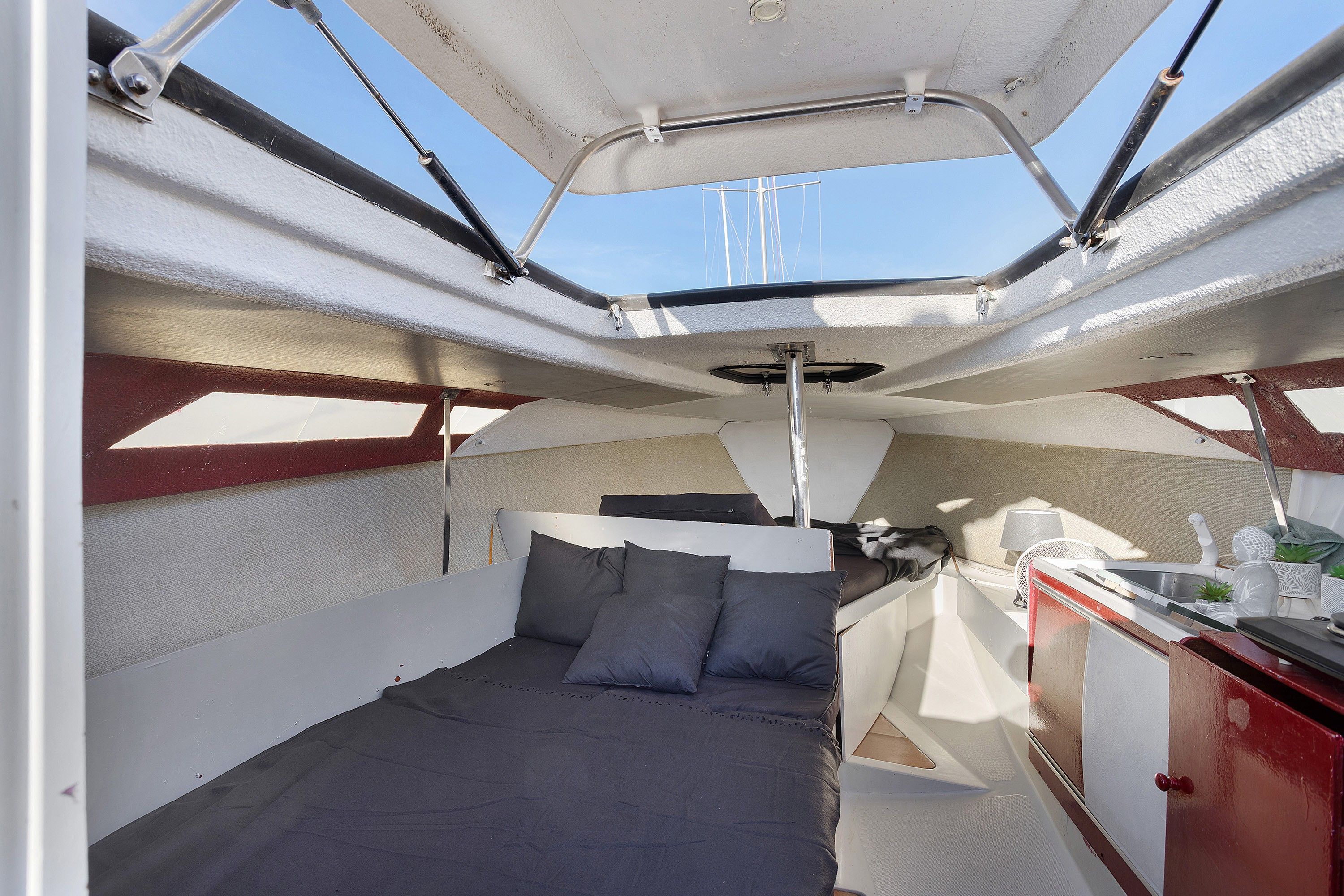 A boat interior with a bed, a small kitchenette, and a view of the sky.