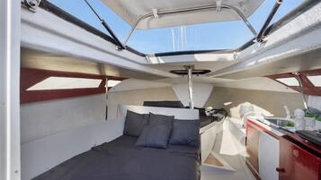 A boat interior with a bed, a small kitchenette, and a view of the sky.