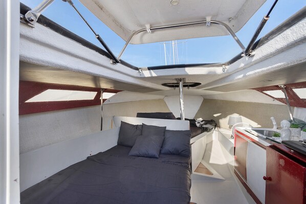 L'intérieur d'un bateau, avec un lit, une petite cuisine et une vue sur le ciel.