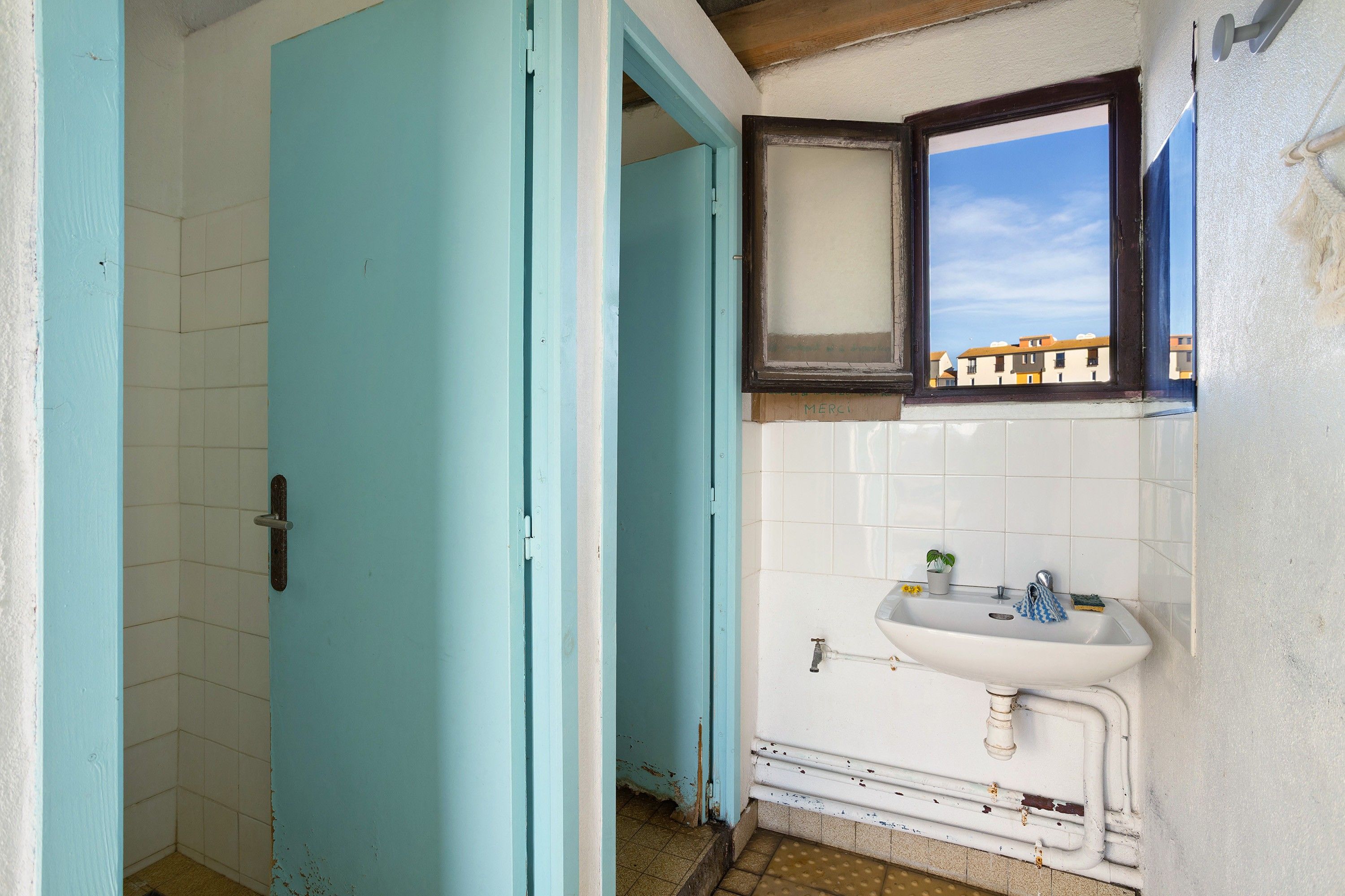 Een badkamer met een wit wastafelmeubel, een raam en een blauwe deur.