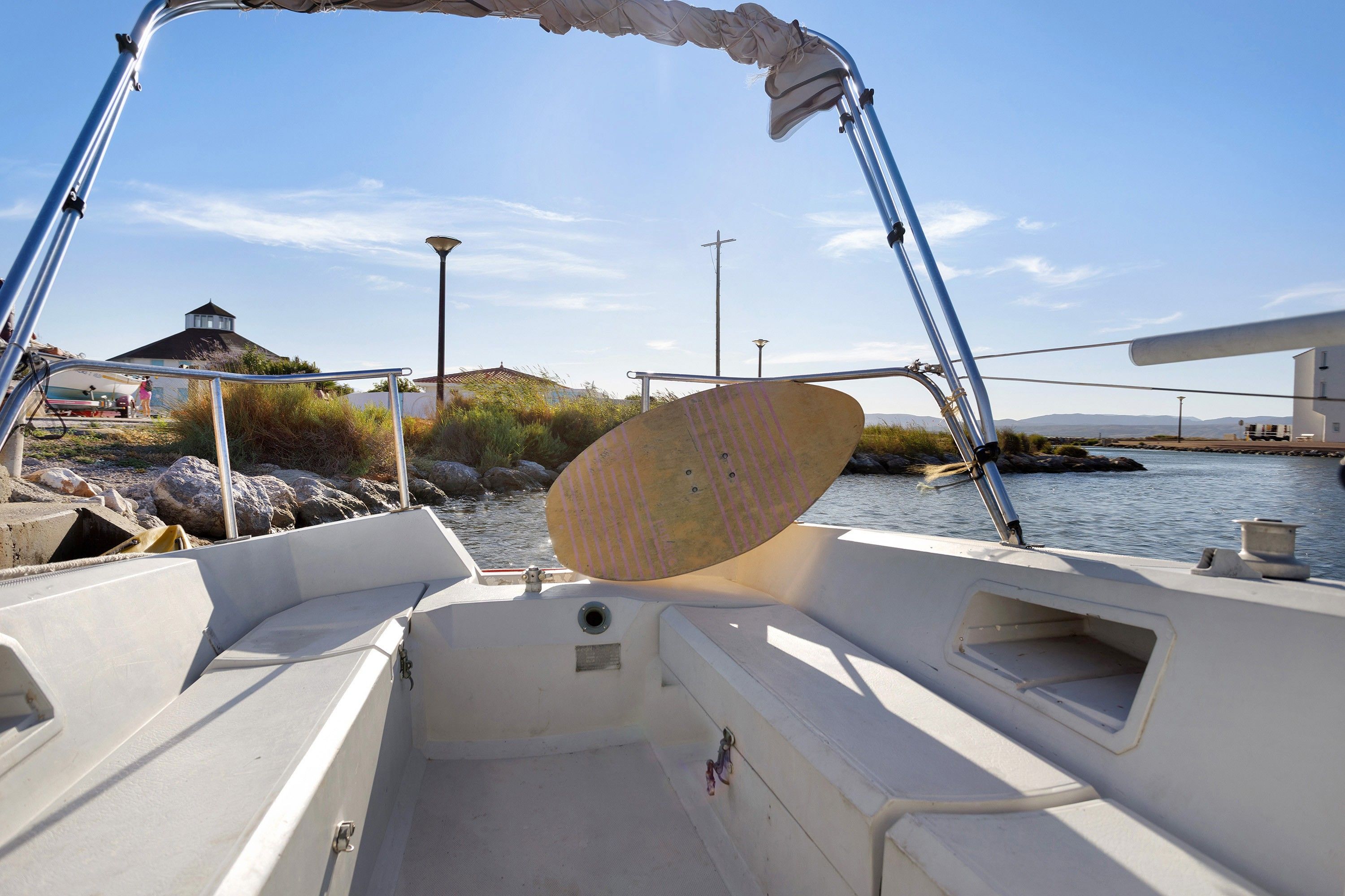 Het interieur van een boot, met een metalen leuning, een bekleed zitje en uitzicht op een rustig wateroppervlak met een verre kustlijn.