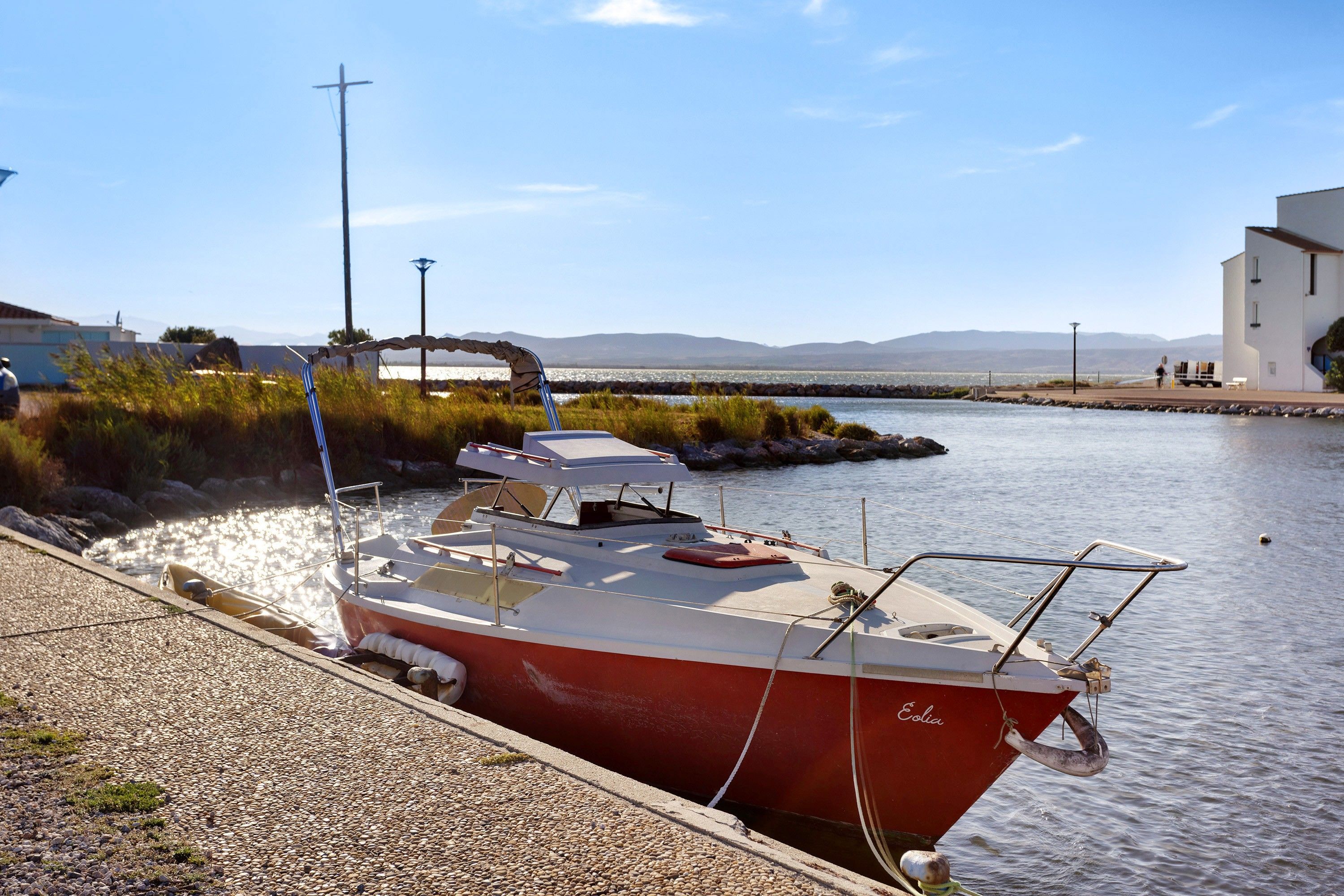 Un bateau rouge était amarré dans une marina, sous un ciel dégagé, avec des montagnes qui se dessinaient à l’horizon.