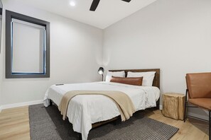 Ein modernes Schlafzimmer mit einem großen Bett, einem Holzkopfstück, einer Nachttischlampe und einem kleinen Holzschemel.