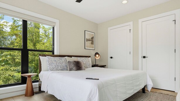 A bedroom with a large window, a bed with white bedding, a bedside lamp, and a framed picture on the wall. - Indoor Pool, Hot Tub & Mountain Views Near Pigeon Forge (Sevierville)