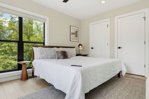 A bedroom with a large window, a bed with white bedding, a bedside lamp, and a framed picture on the wall. - Indoor Pool, Hot Tub & Mountain Views Near Pigeon Forge (Sevierville)