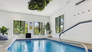 En inomhuspool med stora fönster, en sittgrupp vid poolkanten och en växt som hänger ner från taket.
