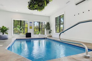 An indoor swimming pool with clear windows, a poolside seating area, and a ceiling-mounted plant. - Indoor Pool, Hot Tub & Mountain Views Near Pigeon Forge (Sevierville)