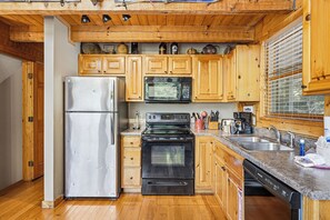 A compact kitchen with a stainless steel refrigerator, a microwave, an oven, and a dishwasher. Wooden cabinets and a granite countertop are also visible. - Smoky Mountain Views, Hot Tub & Game Loft Retreat (PIGEON FORGE)