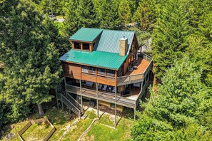 Een chalet met meerdere verdiepingen en een groen dak, omringd door een dicht bos.