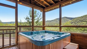 Un bain à remous sur une terrasse en bois, avec vue sur une chaîne de montagnes boisées.