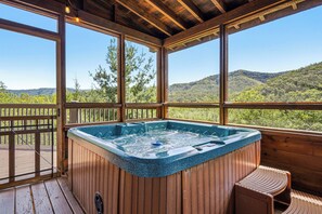 Een hottub op een houten terras met uitzicht op een bebost gebergte.