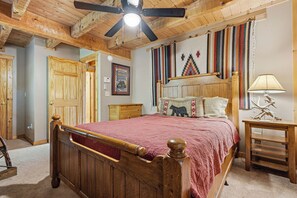 A bedroom with a wooden bed, a ceiling fan, a nightstand, a lamp, and a wall with a colorful tapestry. - Smoky Mountain Views, Hot Tub & Game Loft Retreat (PIGEON FORGE)