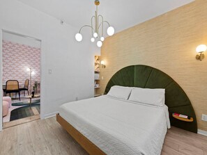 Ein Schlafzimmer mit einem Bett, einer gewölbten Kopfteil, einer Wandleuchte und einem kleinen Regal.