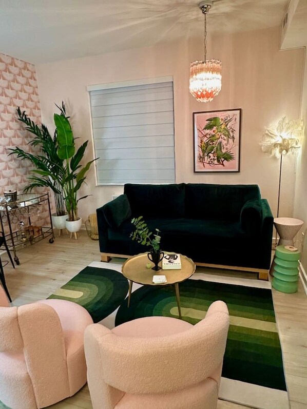 Ein Wohnzimmer mit einem dunkelgrünen Sofa, einem runden Couchtisch und einer großen Kübelpflanze.