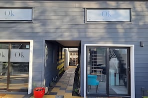A building facade with 'Ok' signs above the entrance doors, a pathway leading to a covered area, and a blue chair outside. - Okeyloft 2 Coyhaique (Coyhaique)