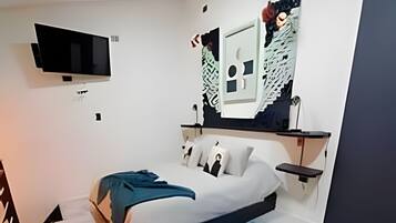 A modern bedroom with a bed, a flat-screen TV mounted on the wall, and a unique wall art piece.