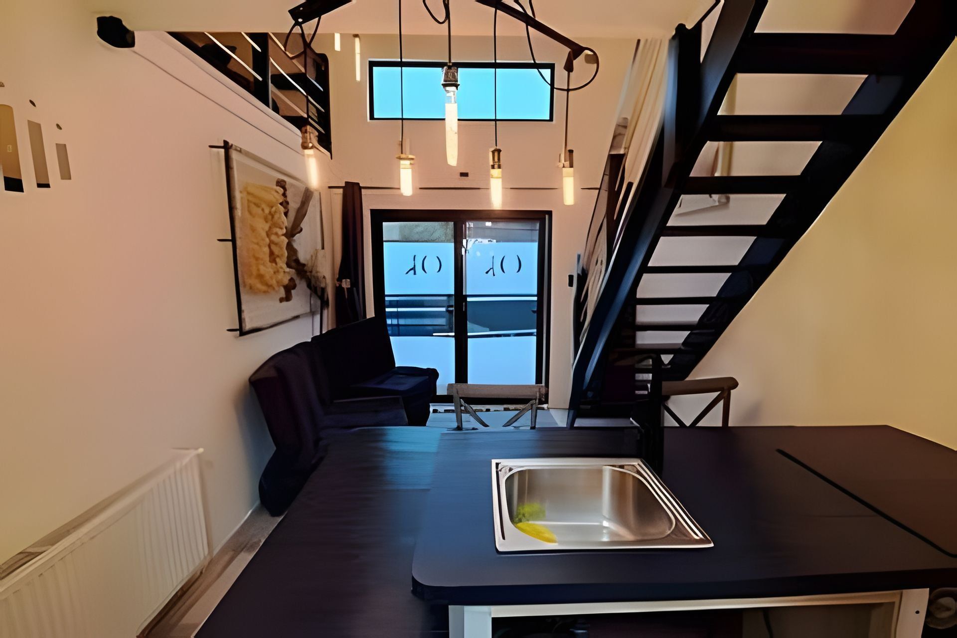 A modern kitchen with a built-in sink, a dark countertop, and a staircase leading to an upper level.