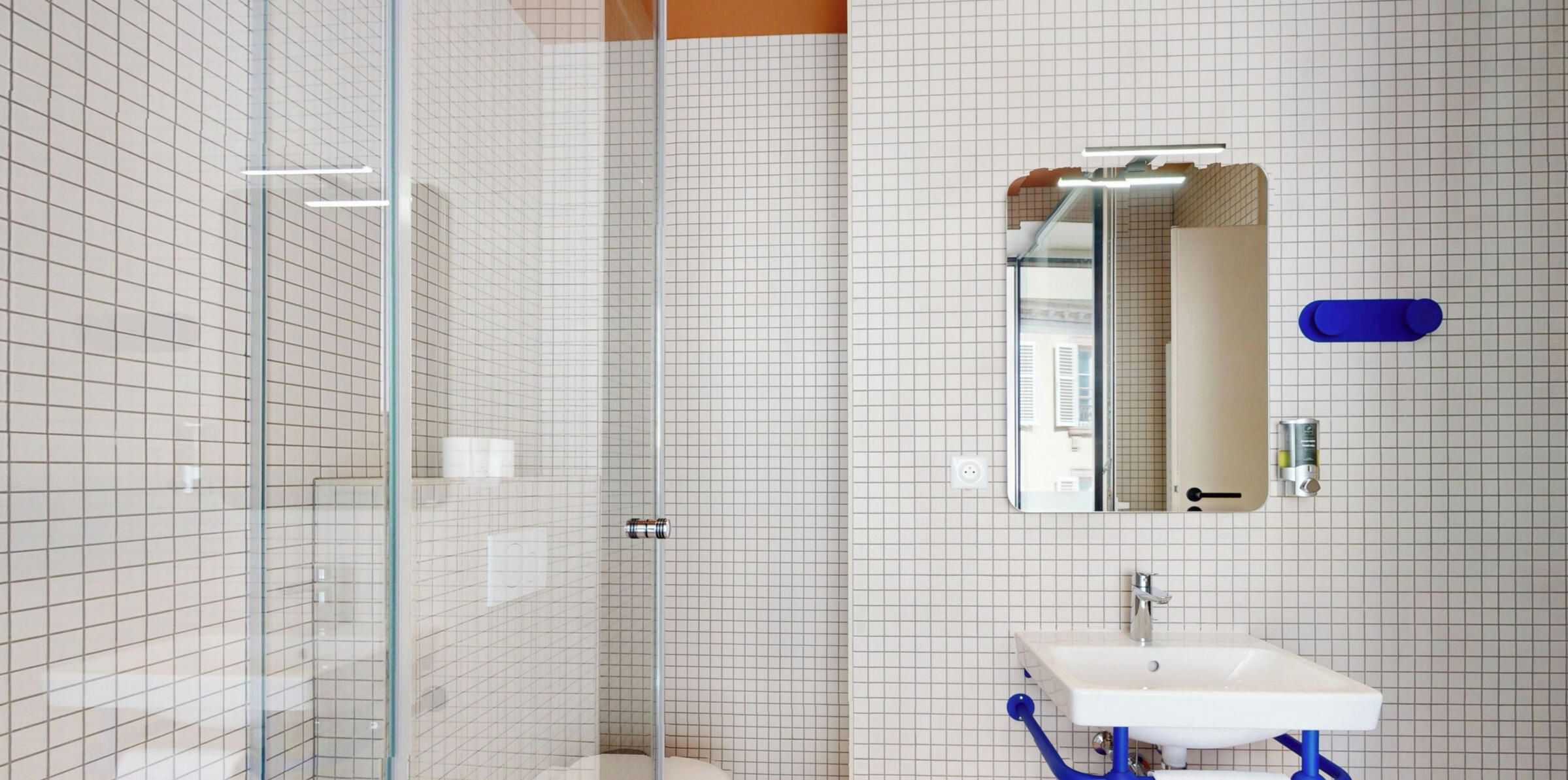 Ein modernes Badezimmer mit einer Duschkabine aus Glas, einem weißen Waschbecken mit blauen Armaturen und einem Spiegel mit Handtuchhalter.